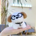 Close-up of plush puppy keychain with black glasses and bell collar held in hand - White Body Brown Ears