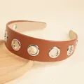 Brown leather headband with silver metal eyelets and non-slip lining on wood stand - Brown