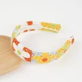 Detailansicht des handgefertigten Häkel-Stirnbands mit bunten gestrickten Gänseblümchen - Orangefarbene Blume