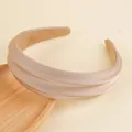 Dettaglio di un cerchietto in raso champagne imbottito su un vassoio di legno con sfondo soft - Cachi
