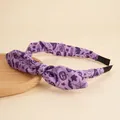 Detail of purple Halloween headband with bat pumpkin print and bow on wooden tray - Purple