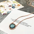 Détail d'un collier en or rose avec une grosse pierre bleue en goutte et un halo de zircons - Or Rose + Bleu Encre