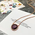 Gros plan d'un collier en or rose avec une pierre violette taillée et cristaux - Or Rose Violet