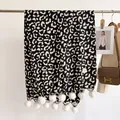Detailed shot of leopard print winter scarf with white pom-poms and COOL brand label - 180x68cm / Black