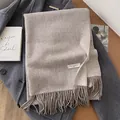 Minimalist oatmeal wool scarf with tassels, draped over a dark grey winter coat - Oatmeal
