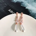 Dettaglio di orecchini lunghi con perle oro rosa e cristalli su un piatto di porcellana - Oro Rosa + Bianco