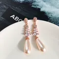 Dettaglio di orecchini lunghi in oro rosa con zirconi e pendenti di perle a goccia - Oro Rosa e Champagne
