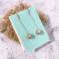 Detail van lange roségouden oorbellen met gepolijste metalen ballen en dunne ketting - Roségoud