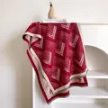 Detail eines rot-beigen Schals mit Chevron-Muster und Fransen auf einem weißen Regal - 185x65cm / Dunkelrot