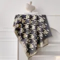 Dettaglio dello scialle pied de poule grigio con frange appeso a uno scaffale bianco - 185x65cm / Grigio
