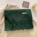 Dark green wool blend scarf with fringe tassels laid flat on a beige coat surface - 211x31cm / Dark Green