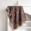 Close-up of deep brown paisley printed scarf with fringe tassels on a minimalist shelf - 185x65cm / Coffee