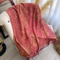 Detail of red paisley shawl with gold patterns and fringe on a soft armchair - Red