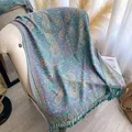 Detail of teal paisley pattern shawl with fringe draping over a beige sofa - Teal