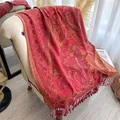 Détail d'un châle cachemire rouge à motifs paisley dorés et pompons sur un fauteuil - Rouge