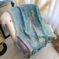 Dettaglio di sciarpa jacquard con motivo paisley e morbide nappe su un divano crema - Verde petrolio