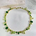 Detaillierte Draufsicht einer goldenen Kette mit grünen Kristallen auf weißer Textur - Grün