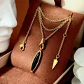 Dettaglio collana dorata con pendente ovale in onice nera su supporto in velluto marrone - Collana con pendente a goccia d'acqua / Color Agata Nera
