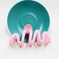Dettaglio del fermaglio per capelli rosa a onde con finitura lucida su piatto verde - Rosa