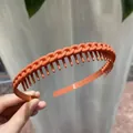 Handheld view of an orange chain-textured headband with inner teeth for secure hair styling - Orange