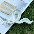 Pinza de pelo acrílica color crema ondulada sobre revista en un fondo de césped - Blanco