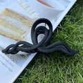 Pinza para el pelo grande negra mate con diseño ondulado sobre una revista al aire libre - Negro