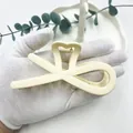 Dettaglio di una pinza per capelli opaca color crema con design a incrocio e molla robusta - Avorio