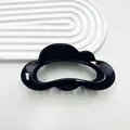 Macro detail of a glossy black cloud-shaped hair claw clip on a white textured tray - Bright Black