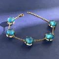 Detailed macro of gold bracelet featuring five vibrant blue crystals on a textured blue surface - Gold (Sea Blue + Clear)
