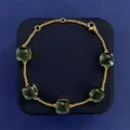 Macro shot of gold bracelet featuring five square-cut green gems with lobster clasp detail - Gold and Navy Blue