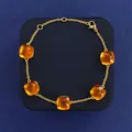 Gold chain bracelet with five square orange gemstones on blue jewelry display pad - Gold+Ochre