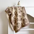 Detail of cashmere-feel leopard print scarf with fringe edges draped on furniture - Camel