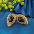 Vintage gold textured earrings featuring black oval gemstones on blue velvet display - Bronze And Black