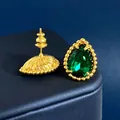 Gros plan de boucles d'oreilles goutte dorées avec pierres vertes sur soie bleue - Or + Vert Malachite