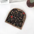Detailed close-up of brown knit beanie featuring black graffiti lettering and red stars - One Size / Coffee