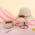 Detail eines Strohhuts und einer Tasche für Kinder mit drei roten Erdbeer-Dekorationen - Beige