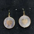 Detail van ronde rozenkwarts oorbellen met gouden hart op een zwarte display - Hartstijl