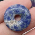 Natural blue and white sodalite stone donut pendant shown on a fingertip for scale - Blue Spot Stone