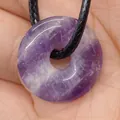 Pendentif donut en améthyste violette naturelle avec cordon noir tenu dans la main - Améthyste
