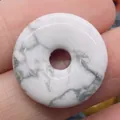 Polished white marble donut pendant with grey veins held between fingers for size - Howlite