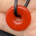 Pendentif donut en agate rouge avec un cordon noir tressé posé sur la main - Agate rouge