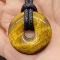 Tiger's eye gemstone donut pendant on black braided cord held in hand for scale - Tiger's Eye
