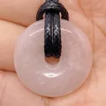 Pink rose quartz donut pendant on a black woven cord held in a person's hand - Rose Quartz