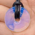 Translucent opalite stone donut pendant on a black cord shown being held in hand - Opal