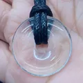 Handheld view of a 20mm clear quartz donut pendant with black braided cord necklace - Transparent Crystal