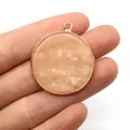 Pendente rotondo in pietra rosa marmorizzata con bordo dorato tenuto tra le dita - Avventurina Rosa / 30mm, 8g