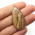 Teardrop picture jasper stone pendant with gold metal rim held in hand - Picture Jasper
