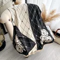 Detail of camellia floral knit shawl with fringes and diamond grid pattern on sofa - Black