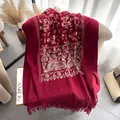 Ethnic burgundy shawl with floral paisley embroidery and tassels on a soft sofa - 185cm / Red