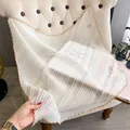 Elegant white pleated silk scarf with golden piping displayed on a beige sofa - Large Square / White